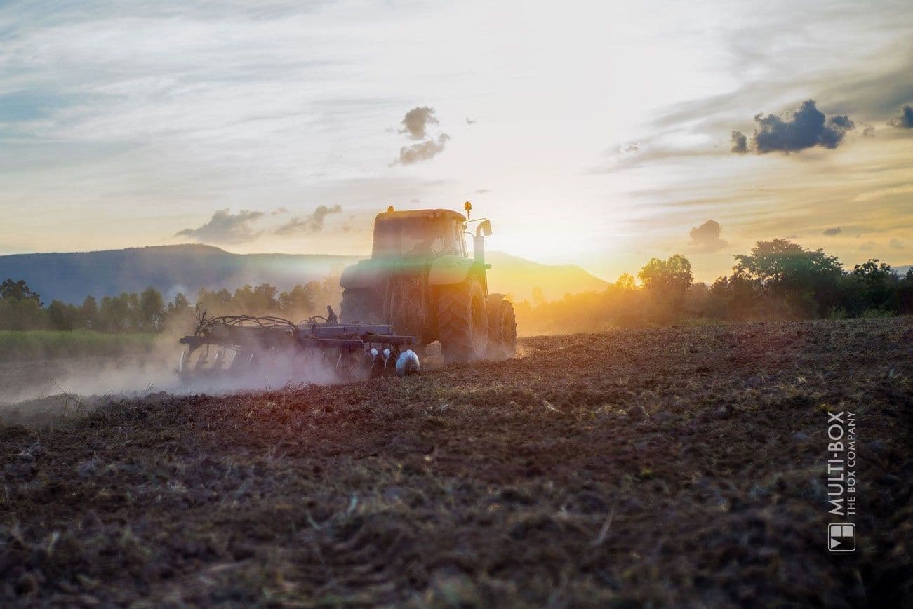 A tractor plows a field at sunset, surrounded by a rural landscape.